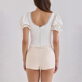 Model wearing House of CB ivory puff-sleeve crop top with lace trim and corset-style back, styled with pale pink mini shorts.