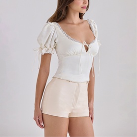 Model wearing House of CB ivory puff sleeve crop top with lace trim and tie detail, styled with cream shorts