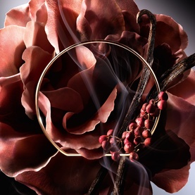 Lanc&ocirc;me Hidden By A Rose Eau De Parfum bottle nestled among deep red rose petals, dark berries, and vanilla pods with soft smoke wisps