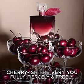 Lanc&ocirc;me EDP in deep cherry-red bottle displayed on stacked coupe glasses filled with fresh cherries, with pink bow detail