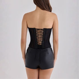 Model wearing House of CB black strapless corset top with lace-up back detail, styled with black mini shorts.