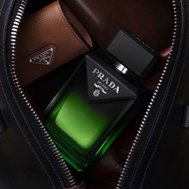 Prada Paradoxe Homme Parfum in deep green glass bottle with black cap, resting inside an open leather bag