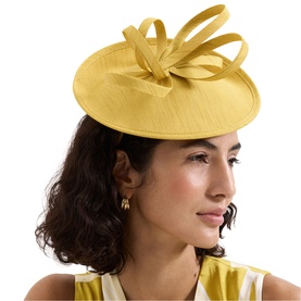 Model wearing Phase Eight yellow sinamay fascinator with looped bow detail, styled with gold drop earrings and yellow dress