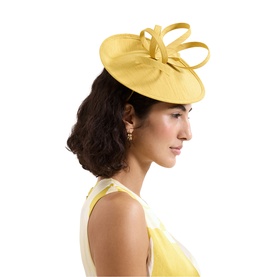 Model with Phase Eight yellow sinamay fascinator hat, featuring loop bow detail, styled with matching yellow dress and pearl earrings
