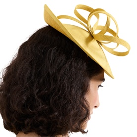Model with Phase 8 yellow fascinator hat featuring looped ribbon detail, worn tilted on dark curly hair, side profile view.