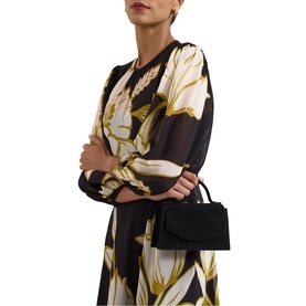 Model carrying black structured top-handle mini bag with flap closure, styled with a black and gold floral print dress