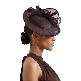 Model wearing Phase Eight brown sinamay fascinator hat with bow and feather trim detail, paired with brown halterneck top