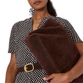 Model carrying Whistles brown suede oversized clutch bag with gold buckle detail, styled with a brown polka dot dress and matching belt.