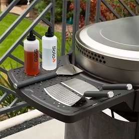 Solo Stove grey side shelf table attached to a grill, styled with condiment bottles and grilling utensils, outdoor patio setting