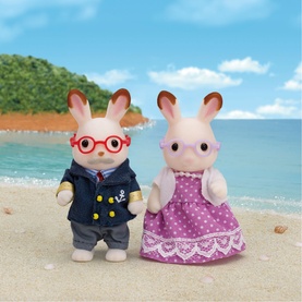 Sylvanian Families chocolate rabbit grandparent figures, grandpa in navy jacket with glasses and grandma in purple polka dot dress, on beach backdrop