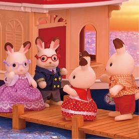 Sylvanian Families rabbit figures in multi-coloured outfits posed on a wooden dock beside a pink boat at sunset