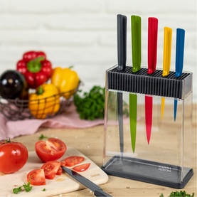 Kuhn Colori Seven-Piece Knife Block Set with multicoloured handles in clear acrylic block, styled on kitchen counter with vegetables and chopping