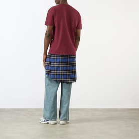 Model wearing Pellador maroon cotton T-shirt, styled with blue tartan wrap skirt and light-wash wide-leg jeans. Rear view.