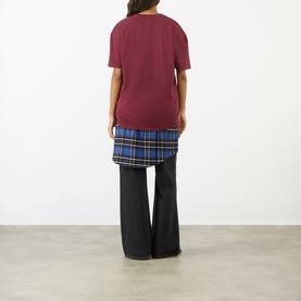 Model wearing Pellador Nutmeg Tonal Logo T-Shirt in maroon, styled with blue tartan skirt and wide-leg grey trousers, back view.