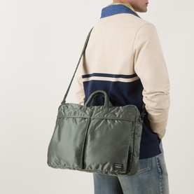 Model carrying Porter Yoshida Tanker 2Way Document Briefcase in sage green nylon, worn crossbody, styled with cream sweater and jeans