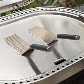 Stainless steel BBQ spatula, scraper and roller tool set with grey handles, resting on a silver griddle surface