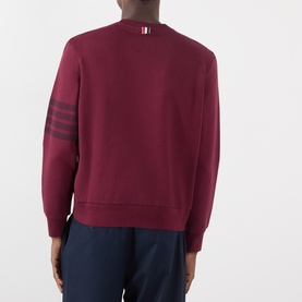 Model wearing Thom Browne burgundy cotton sweatshirt, back view, with tonal 4-bar stripe detail on left sleeve and grosgrain tab at collar.