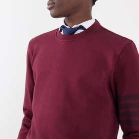 Model wearing Thom Browne burgundy cotton sweatshirt with tonal 4-bar sleeve stripe, styled with white shirt and navy tie.