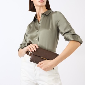 Model carrying Wandler Ida Trio Crossbody Bag in Soil Caviar, dark brown leather with gold-toned clasp, styled with sage satin shirt and white