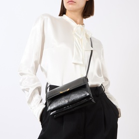 Model carrying Wandler Ida Trio Crossbody Bag in Black Glaze leather, gold-toned clasp, worn cross-body with white ruffled blouse and black trousers