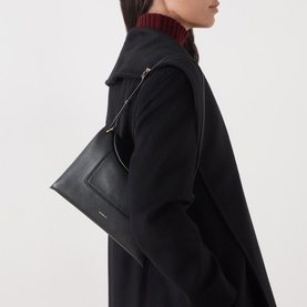 Model carrying Wandler Penelope Slouch Shoulder Bag in Black Crust pebbled leather with gold-toned hardware, styled with black coat.
