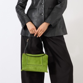 Model carrying Wandler Penelope Suede Slouch Shoulder Bag in Verde Suede, with gold-tone hardware, styled with black wide-leg trousers and leather