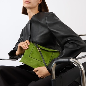 Model carrying Wandler Penelope Suede Slouch Shoulder Bag in Verde Suede, with flap closure and silver-tone hardware, styled with black leather jacket