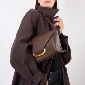 Model carrying Wandler Veneto Shoulder Bag in Soil Caviar with gold-toned hardware and double shoulder strap, styled with brown coat