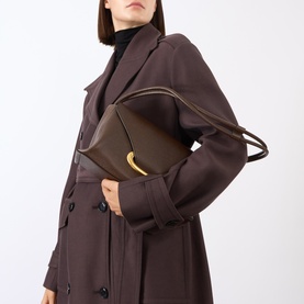 Model carrying Wandler Veneto Shoulder Bag in Soil Caviar with gold-toned hardware and double strap, styled with brown trench coat.