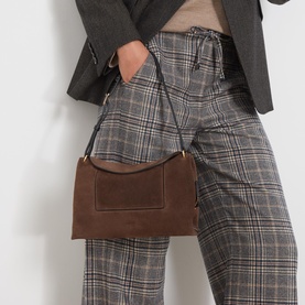 Model carrying Wandler Penelope Suede Slouch Shoulder Bag in Palissander Suede with gold hardware, worn crossbody, styled with plaid trousers and
