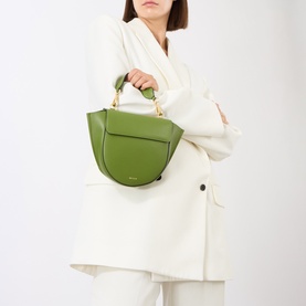 Model carrying Wandler Hortensia Mini Shoulder Bag in verde calf leather, trapeze silhouette with gold-toned hardware and top handle, styled with