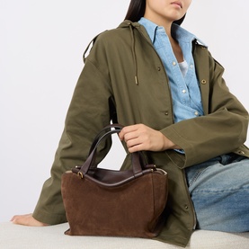 Model carrying Wandler Ida Leather Shoulder Bag in Palissander Suede, double top handles, gold-toned hardware, styled with olive jacket and jeans.