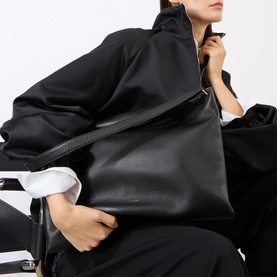 Model carrying Wandler black crust leather tote bag, worn over shoulder, styled with oversized black coat and white shirt