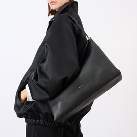 Model carrying Wandler black crust leather tote bag, worn under arm, styled with matching black oversized jacket and trousers