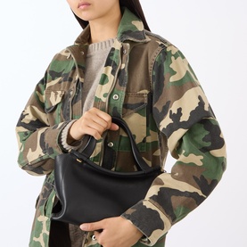 Model carrying a small black structured hobo bag with curved top handle, styled with a green camouflage jacket and grey top.