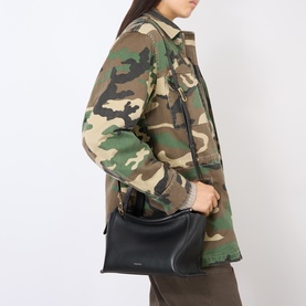 Model carrying a black structured shoulder bag with gold-tone hardware, styled with a camouflage jacket and khaki trousers