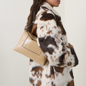 Model carrying Wandler Penelope Slouch Shoulder Bag in Sand Glaze pebbled leather with gold-toned hardware, styled with a cow-print coat.