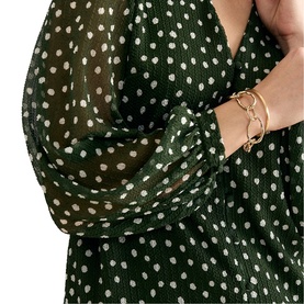 Model wearing Phase Eight green polka dot chiffon dress with voluminous sleeves, styled with a gold chain-link bracelet.