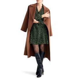 Model wearing Phase Eight green polka dot mini dress, styled with a tan longline coat and black knee-high boots