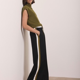 Model wearing Mint Velvet green wide-leg trousers with gold and white side stripe, styled with a khaki sleeveless top.