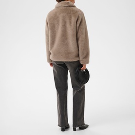 Model wearing Kaffe Rosa Faux Fur Jacket in Taupe Gray, back view, plush cocoon silhouette with stand collar, styled with dark trousers.