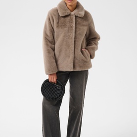 Model wearing Kaffe Rosa Faux Fur Jacket in Taupe Gray, plush cocoon silhouette with stand collar, styled with grey trousers and black round bag.