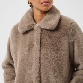 Model wearing Kaffe Rosa Faux Fur Jacket in Taupe Gray, featuring a soft stand collar and plush cocoon silhouette with button fastening.