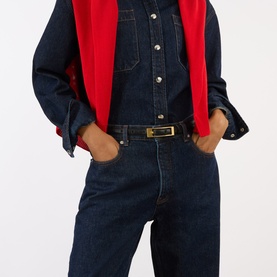 Model with Anine Bing Elly Logo Leather Belt in black, slim smooth leather with gold-toned rectangular logo buckle, styled with dark denim jumpsuit