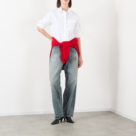 Model wearing Anine Bing white cotton shirt with red knitwear tied at waist, styled with light wash straight-leg jeans and black heeled boots.