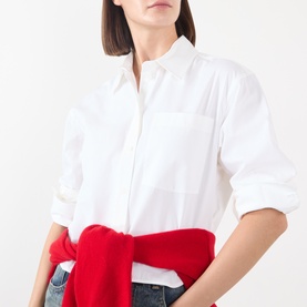 Model wearing Anine Bing white cotton shirt with chest pocket, styled with blue jeans and red knitwear tied at waist.