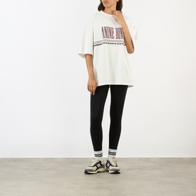 Model wearing Anine Bing white oversized logo cotton T-shirt, styled with black leggings, stripe socks and chunky trainers.