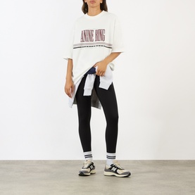 Model wearing Anine Bing white oversized logo T-shirt with black leggings, tied denim shirt, striped socks and trainers.