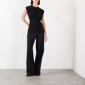 Model wearing Anine Bing black sleeveless top with ruched detail, styled with wide-leg black trousers.