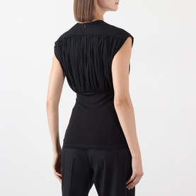 Model wearing Anine Bing black sleeveless top with ruched back detail, styled with black wide-leg trousers, back view shown.